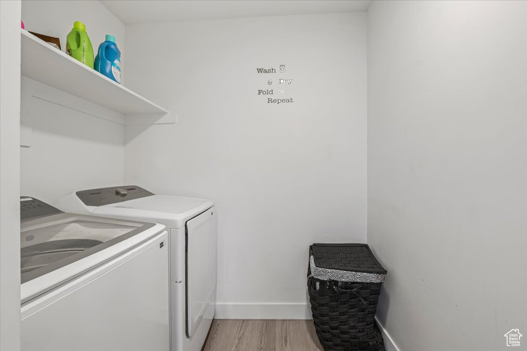 Clothes washing area featuring washer and dryer, light wood-style flooring, laundry area, and baseboards