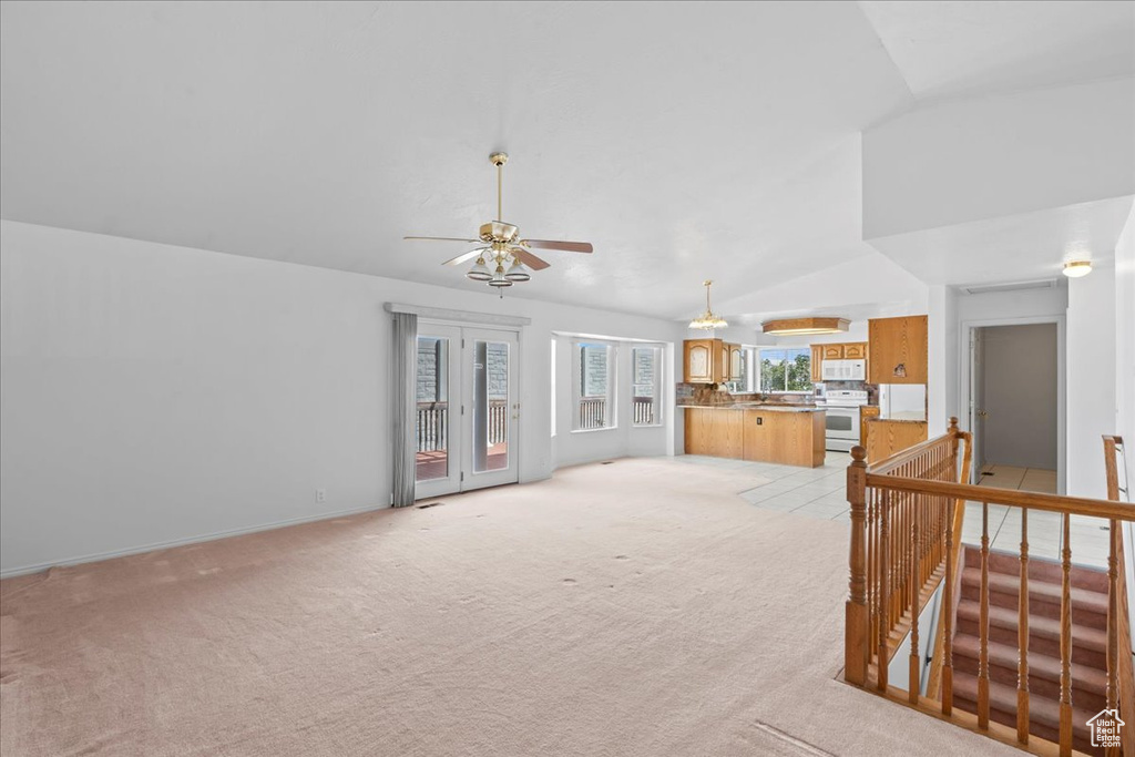 Unfurnished living room with lofted ceiling, light colored carpet, a ceiling fan, and baseboards