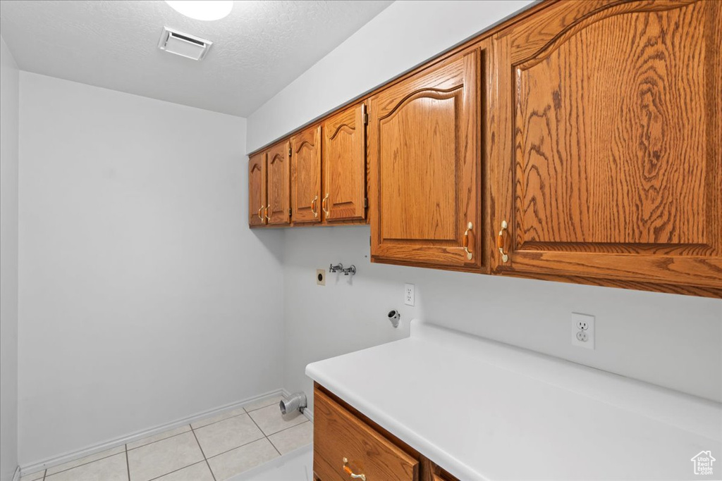 Laundry area with washer hookup, visible vents, baseboards, light tile patterned flooring, and cabinet space