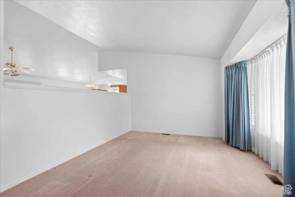 Unfurnished room with ceiling fan, visible vents, vaulted ceiling, baseboards, and light colored carpet