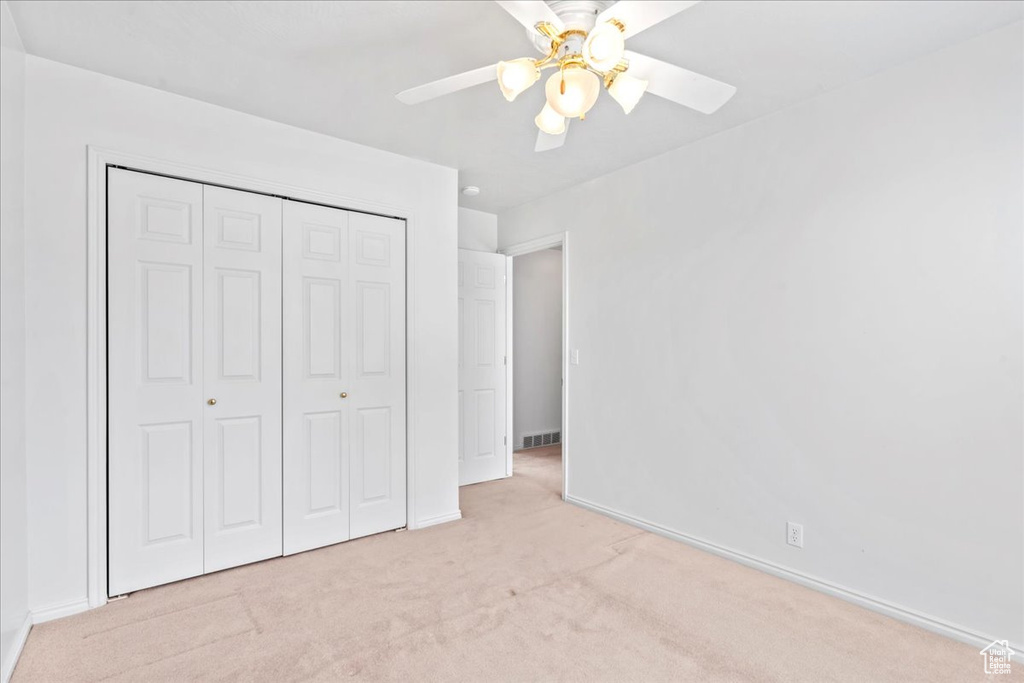 Unfurnished bedroom featuring a closet, light carpet, baseboards, visible vents, and a ceiling fan