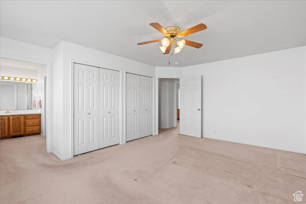 Unfurnished bedroom with a sink, two closets, light colored carpet, and ensuite bath