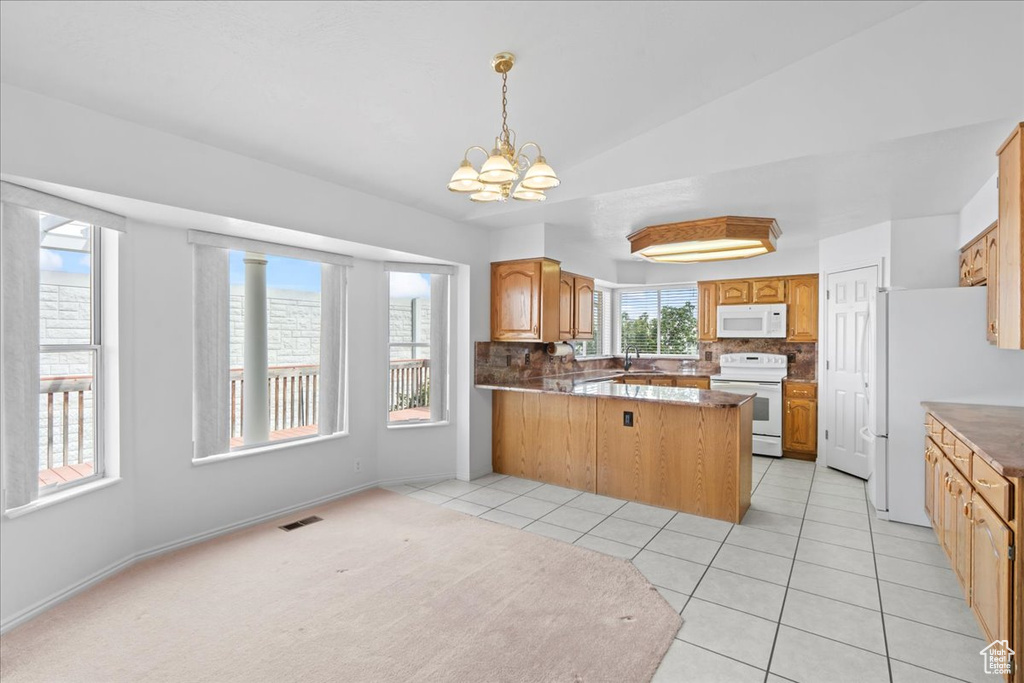 Kitchen with an inviting chandelier, decorative backsplash, a peninsula, white appliances, and lofted ceiling