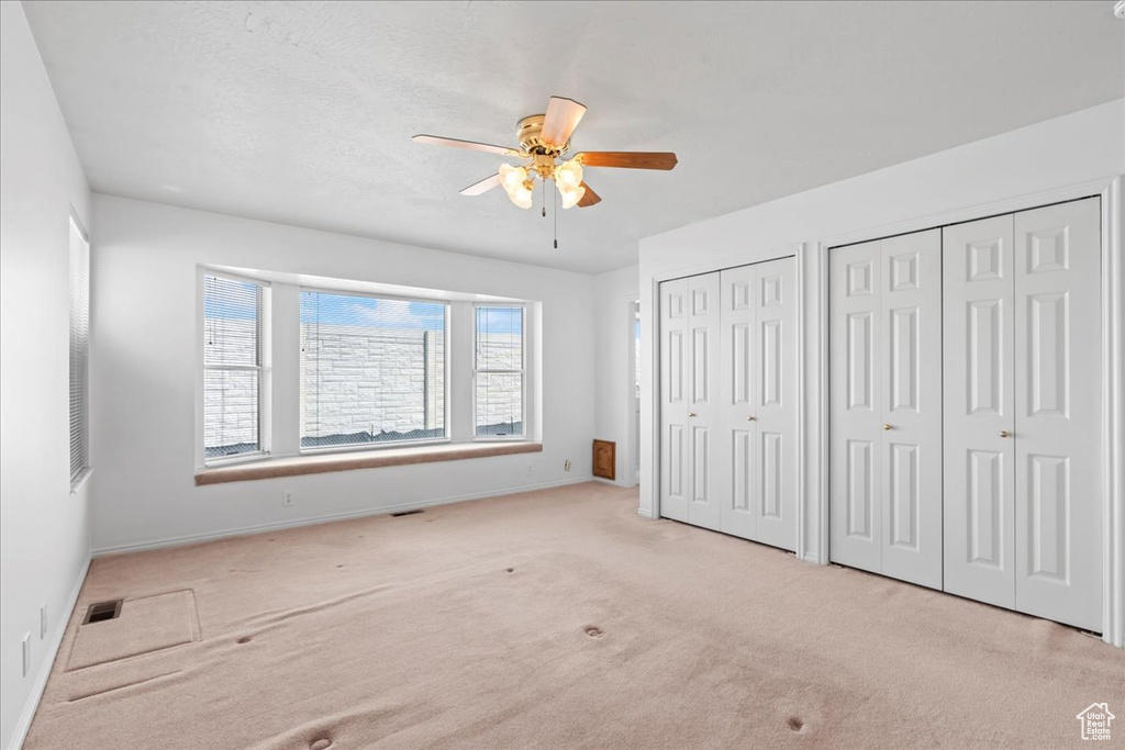 Unfurnished bedroom featuring visible vents, baseboards, carpet, two closets, and a ceiling fan