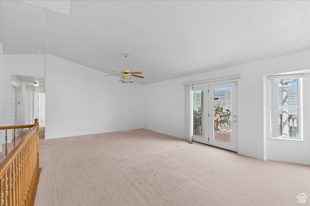 Unfurnished living room with a ceiling fan, a wealth of natural light, lofted ceiling, and light colored carpet