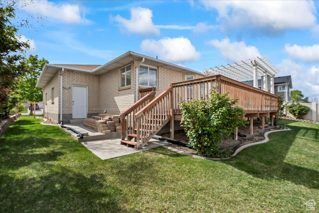 Rear view of property featuring brick siding, a wooden deck, a yard, and stairs