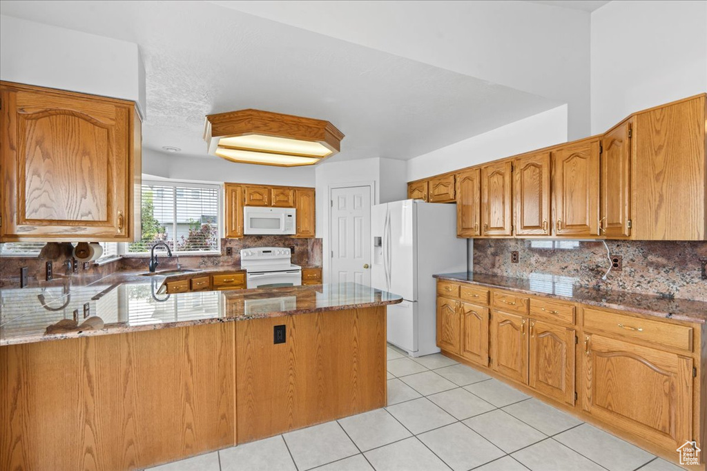 Kitchen featuring a sink, light tile patterned floors, a peninsula, backsplash, and white appliances