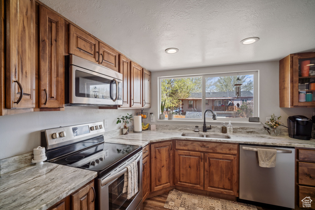 Kitchen with light stone counters, stainless steel appliances, brown cabinets, a sink, and a textured ceiling