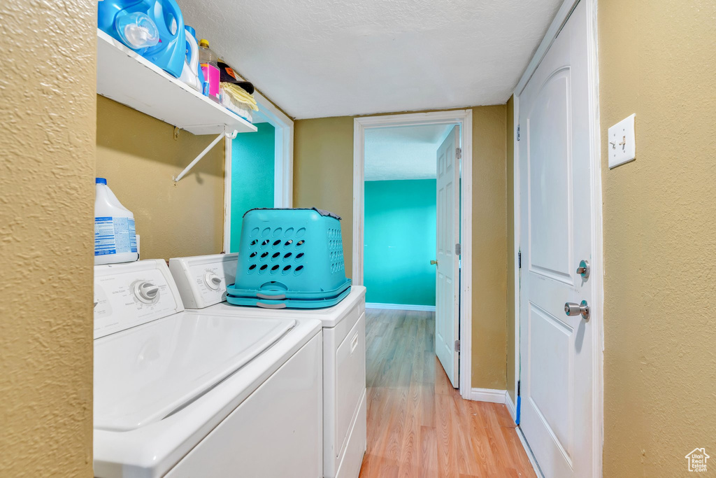 Laundry room featuring a textured ceiling, a textured wall, baseboards, washer and clothes dryer, and light wood finished floors