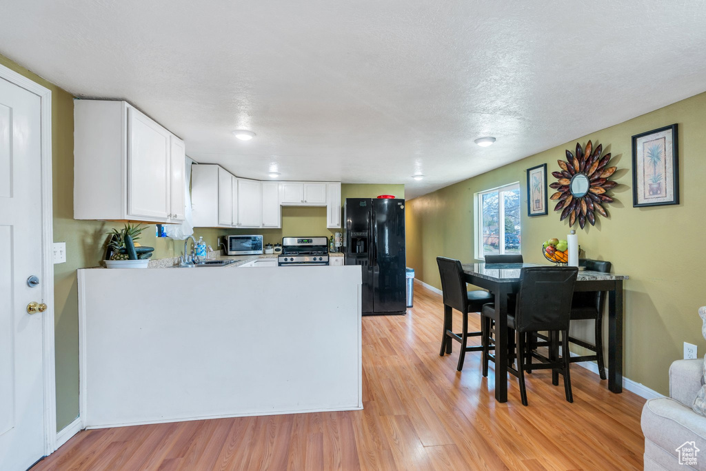 Kitchen with light wood-type flooring, a peninsula, light countertops, white cabinets, and appliances with stainless steel finishes