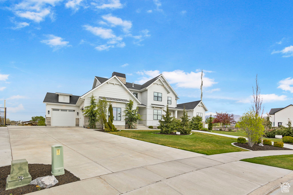 View of front facade featuring a chimney, stone siding, a front lawn, concrete driveway, and an attached garage