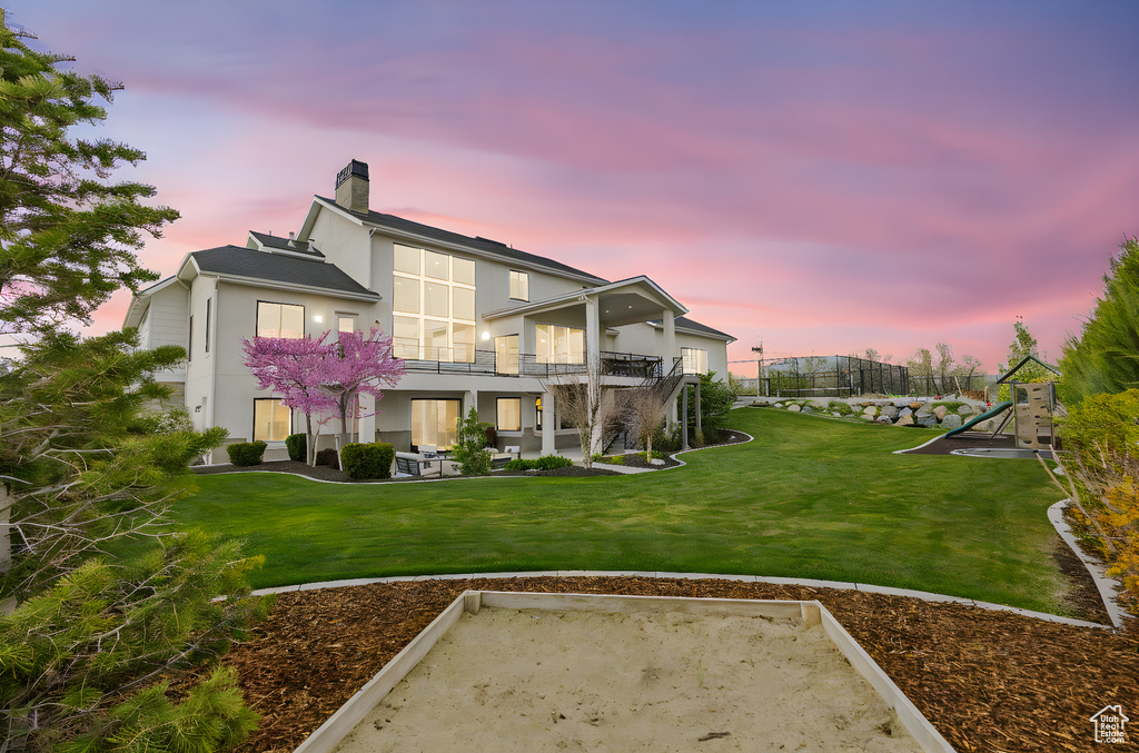 Back of house with a balcony, a patio area, a lawn, a chimney, and stucco siding