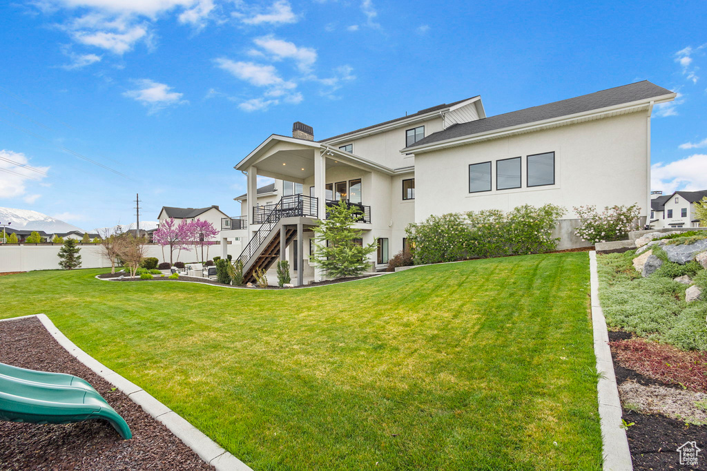 Back of house featuring fence, stairs, a chimney, stucco siding, and a yard