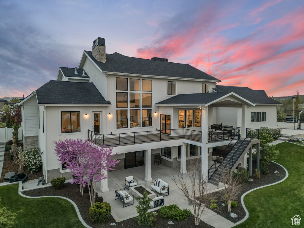 Back of property at dusk with a chimney, a patio area, outdoor lounge area, a shingled roof, and stairway