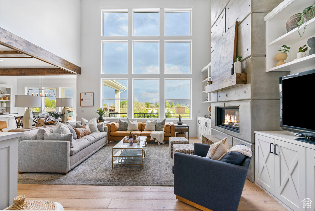 Living area featuring a chandelier, beam ceiling, a glass covered fireplace, light wood finished floors, and a high ceiling