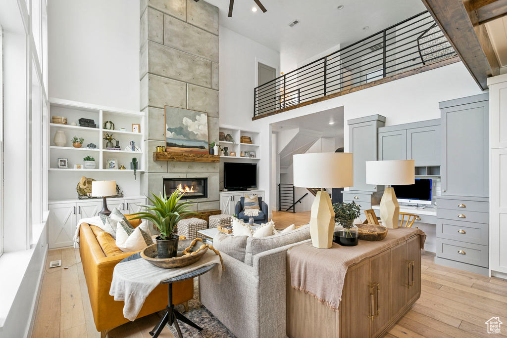Living area featuring a fireplace, light wood-style floors, a ceiling fan, and a high ceiling