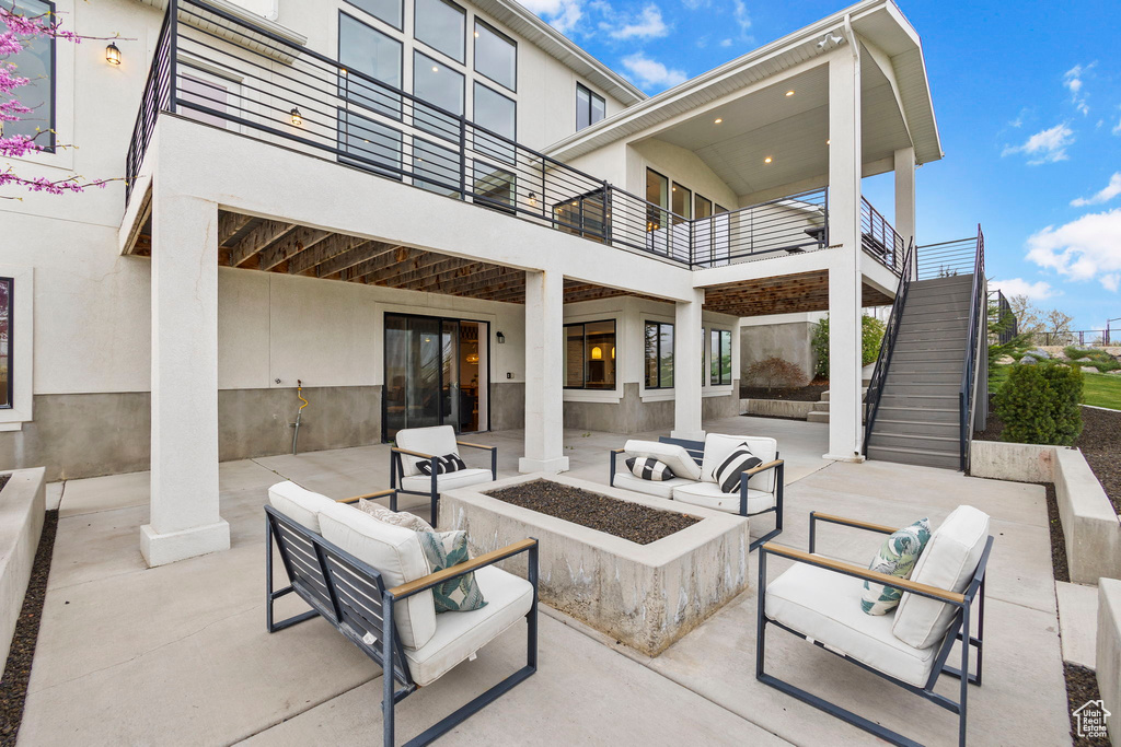 View of patio with an outdoor living space with a fire pit, stairs, and a balcony