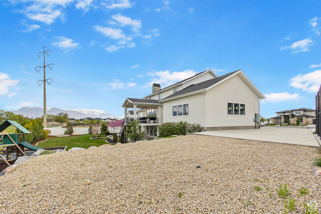 Back of property with fence, a playground, a chimney, a mountain view, and stucco siding