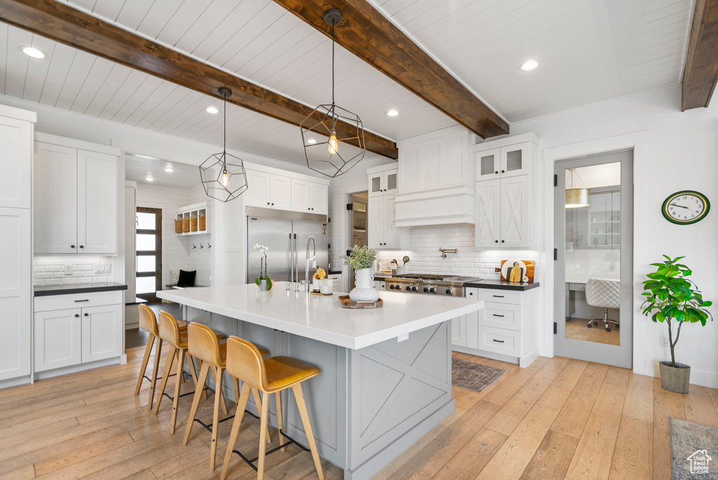 Kitchen with white cabinets, stainless steel appliances, a kitchen bar, light wood-type flooring, and backsplash