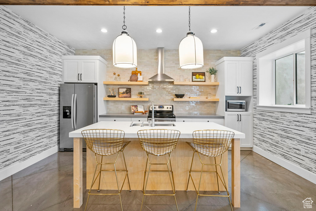 Kitchen with stainless steel appliances, open shelves, wall chimney range hood, a sink, and concrete flooring