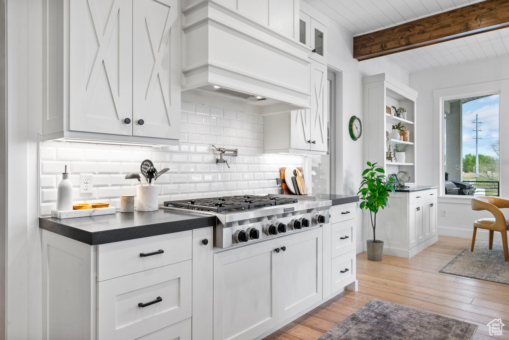 Kitchen featuring beamed ceiling, stainless steel gas stovetop, decorative backsplash, premium range hood, and dark countertops