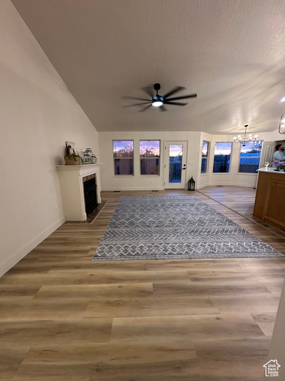 Living area featuring a fireplace with flush hearth, baseboards, a textured ceiling, wood finished floors, and ceiling fan with notable chandelier