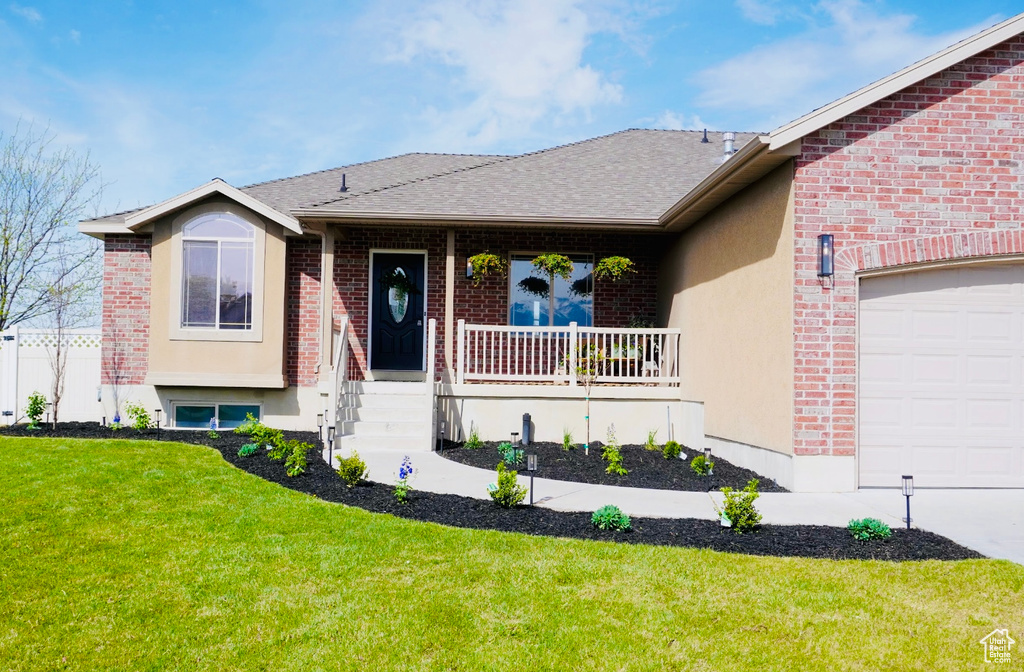 View of front of home with a front lawn, covered porch, an attached garage, and brick siding