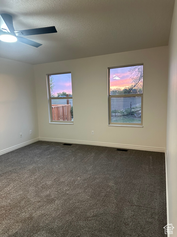 Empty room with baseboards, dark colored carpet, visible vents, and a ceiling fan