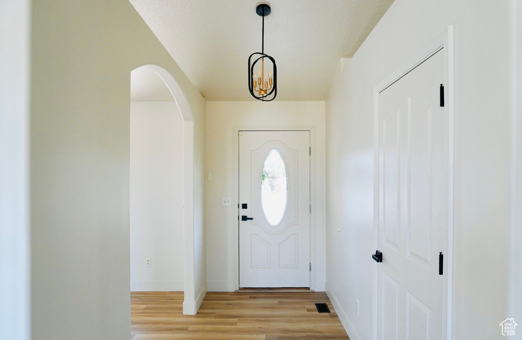 Foyer entrance with arched walkways, visible vents, baseboards, and light wood-style floors