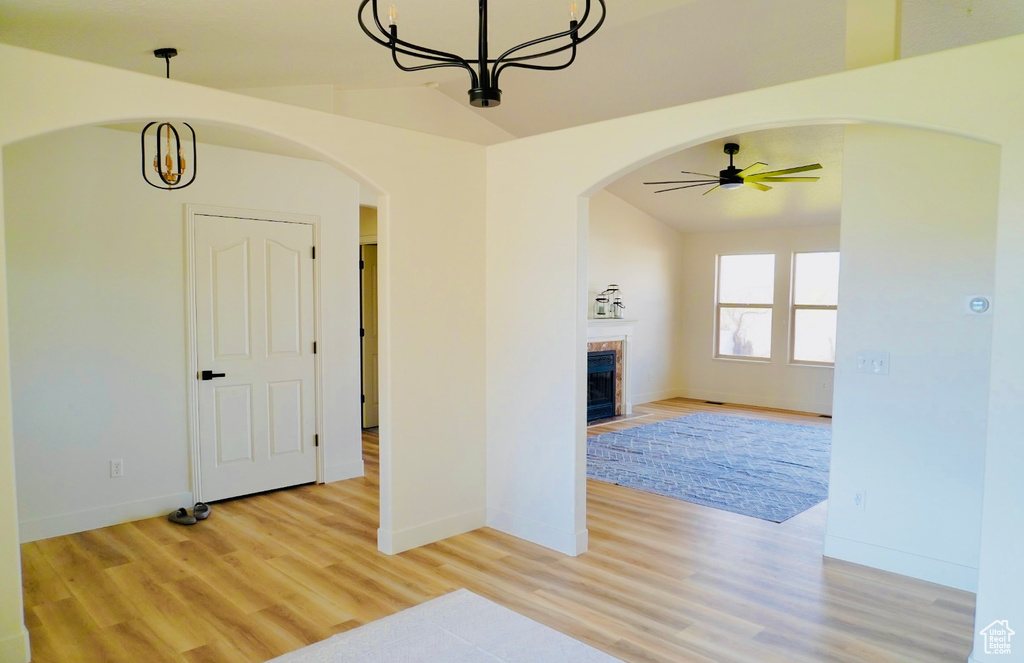 Unfurnished living room with arched walkways, ceiling fan with notable chandelier, and light wood-style floors