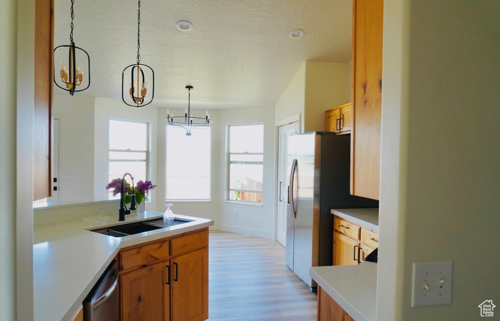 Kitchen with a sink, light wood-style floors, light countertops, an inviting chandelier, and decorative light fixtures