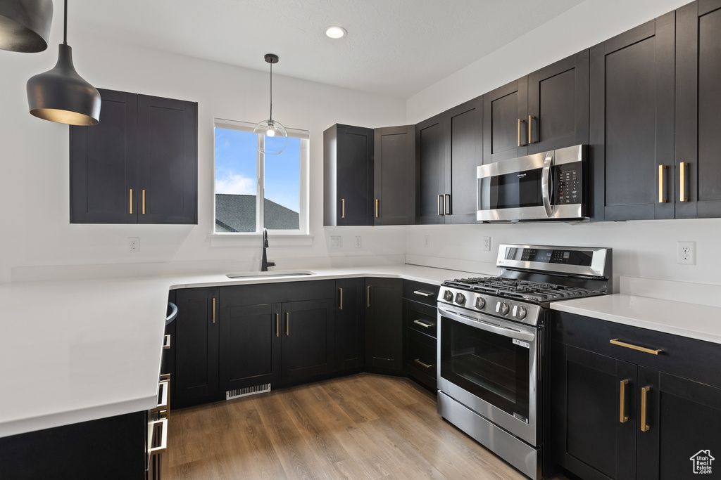 Kitchen featuring dark cabinets, appliances with stainless steel finishes, a sink, recessed lighting, and decorative light fixtures