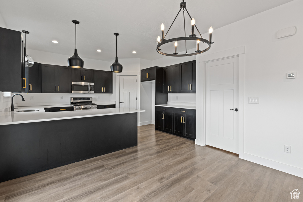 Kitchen with recessed lighting, an inviting chandelier, a sink, appliances with stainless steel finishes, and dark cabinets