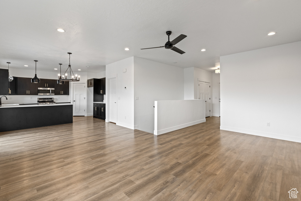Unfurnished living room featuring light wood-type flooring, recessed lighting, baseboards, and ceiling fan with notable chandelier