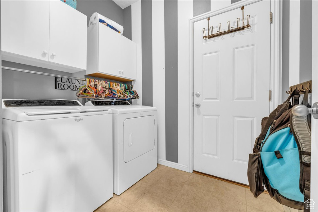Laundry area featuring light tile patterned flooring, washer and clothes dryer, cabinet space, and baseboards