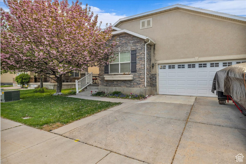 View of front of house with driveway, stone siding, stucco siding, a front lawn, and a garage
