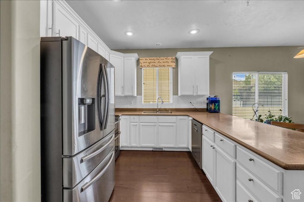 Kitchen featuring white cabinetry, a sink, stainless steel appliances, dark wood-style floors, and a peninsula