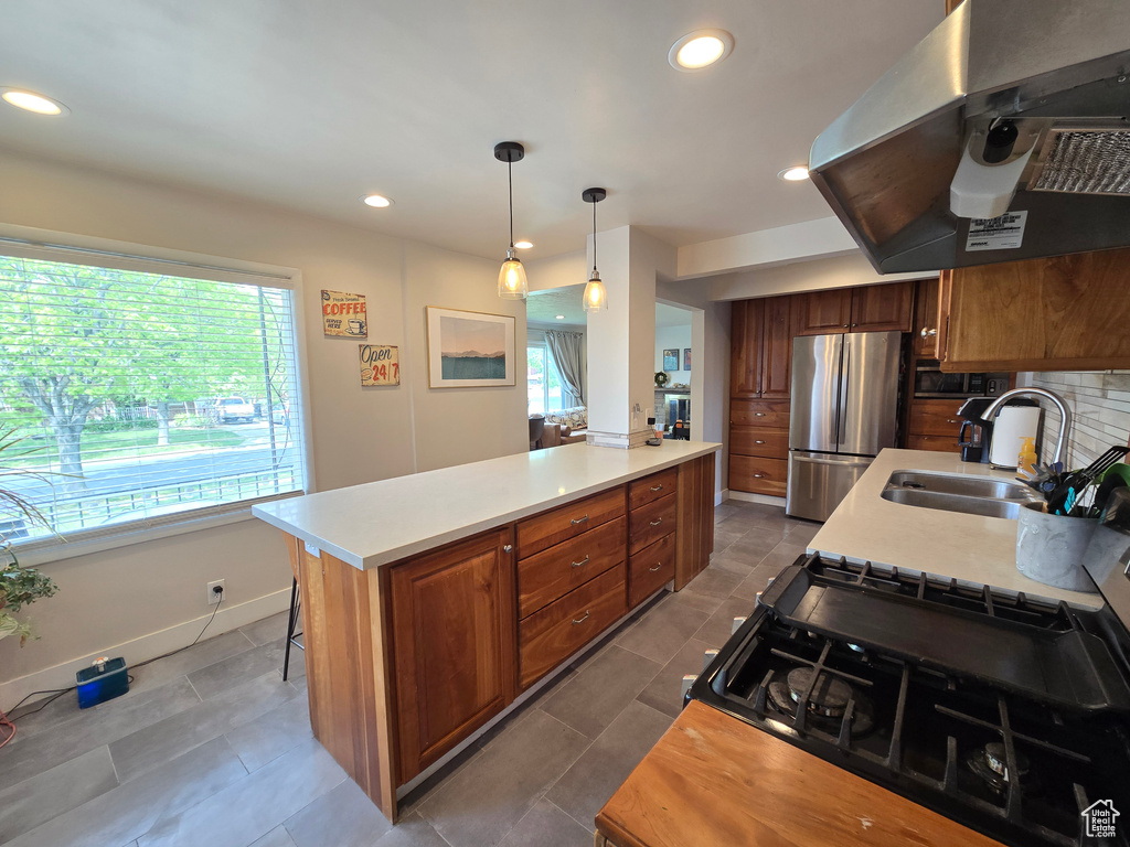 Kitchen featuring brown cabinets, a sink, light countertops, freestanding refrigerator, and range hood