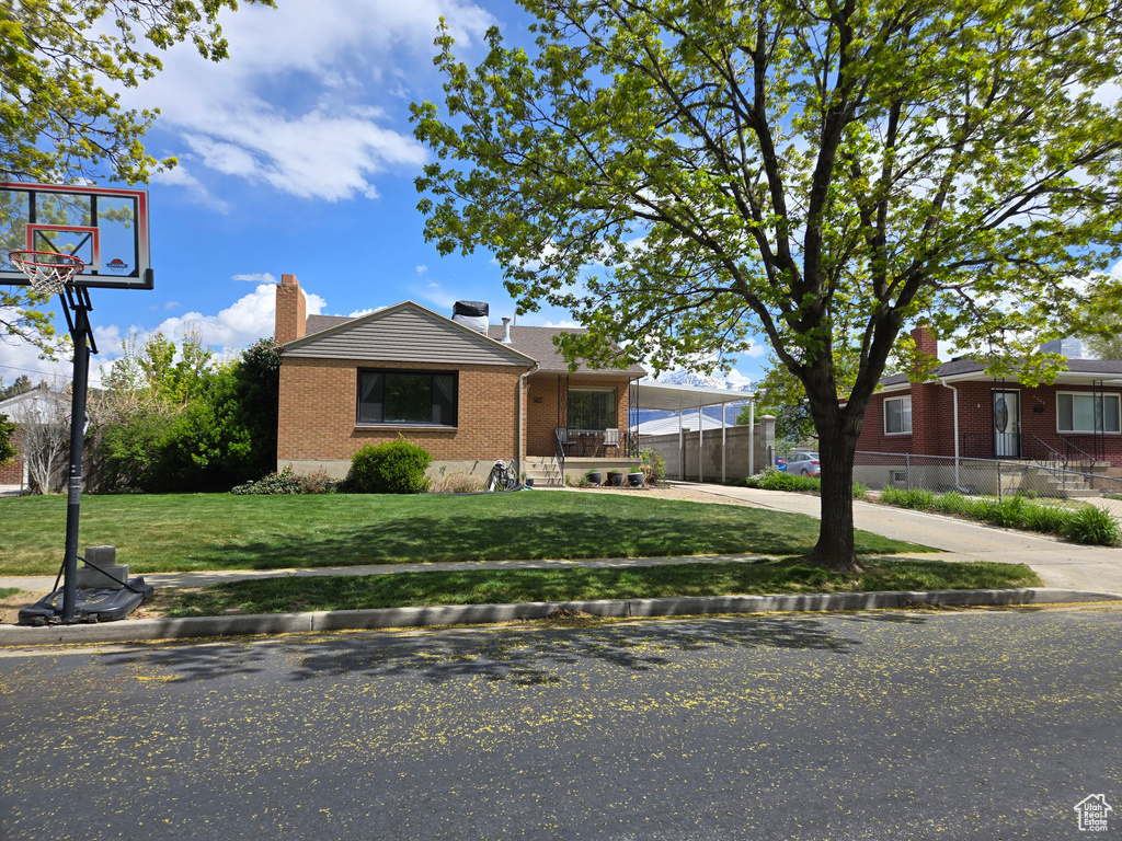 Bungalow-style house featuring driveway, a chimney, fence, brick siding, and a front lawn