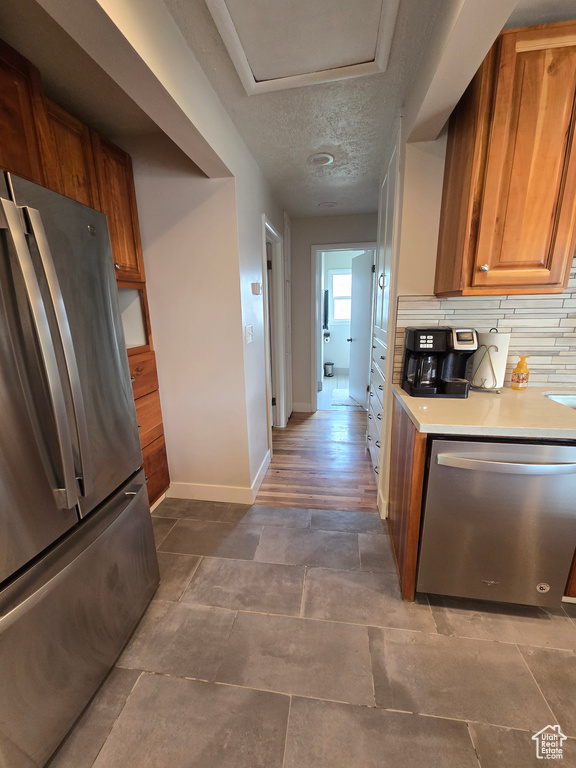 Kitchen with brown cabinets, stainless steel appliances, baseboards, backsplash, and light countertops