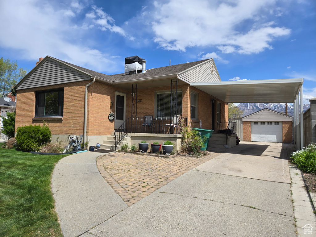 View of front of home featuring covered porch, brick siding, an outbuilding, driveway, and a front lawn