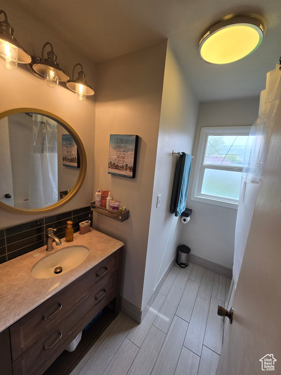 Bathroom with tasteful backsplash, a shower with curtain, wood tiled floor, baseboards, and vanity
