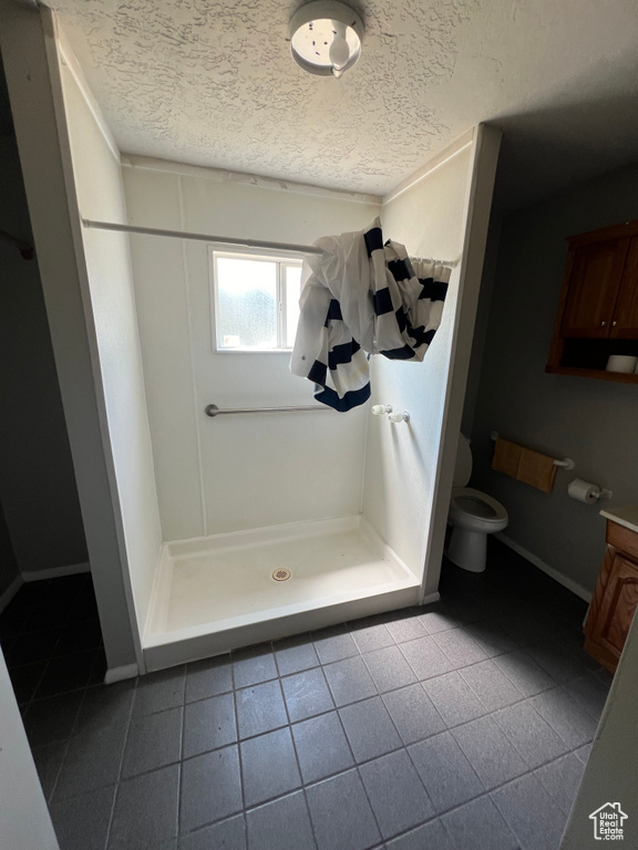 Full bathroom with a textured ceiling, a shower stall, toilet, and tile patterned flooring
