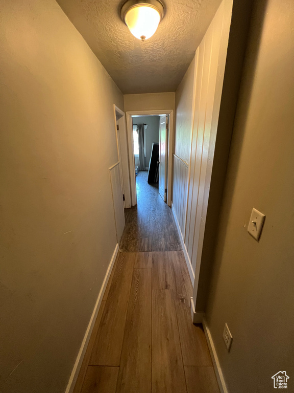 Hall featuring a textured ceiling, wood finished floors, and baseboards