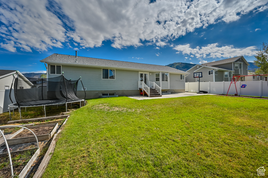 Rear view of property with a trampoline, a fenced backyard, a yard, entry steps, and a patio area