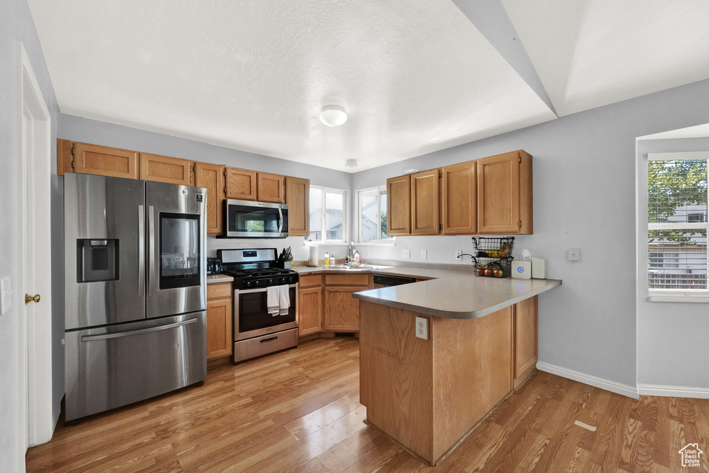 Kitchen with stainless steel appliances, baseboards, light wood-style flooring, a peninsula, and light countertops