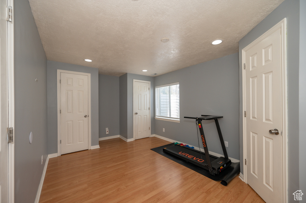 Exercise area featuring recessed lighting, a textured ceiling, light wood-style flooring, and baseboards