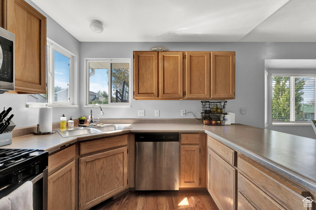Kitchen featuring a sink, light countertops, dishwasher, dark wood finished floors, and gas stove