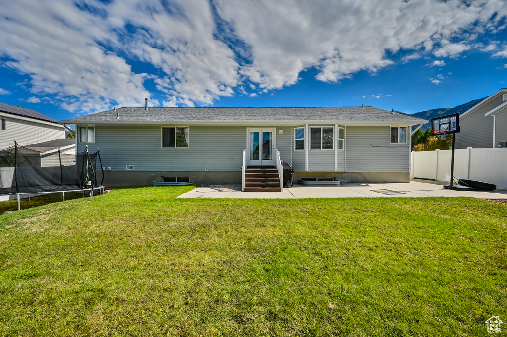 Rear view of property with entry steps, a trampoline, a patio area, fence, and a yard
