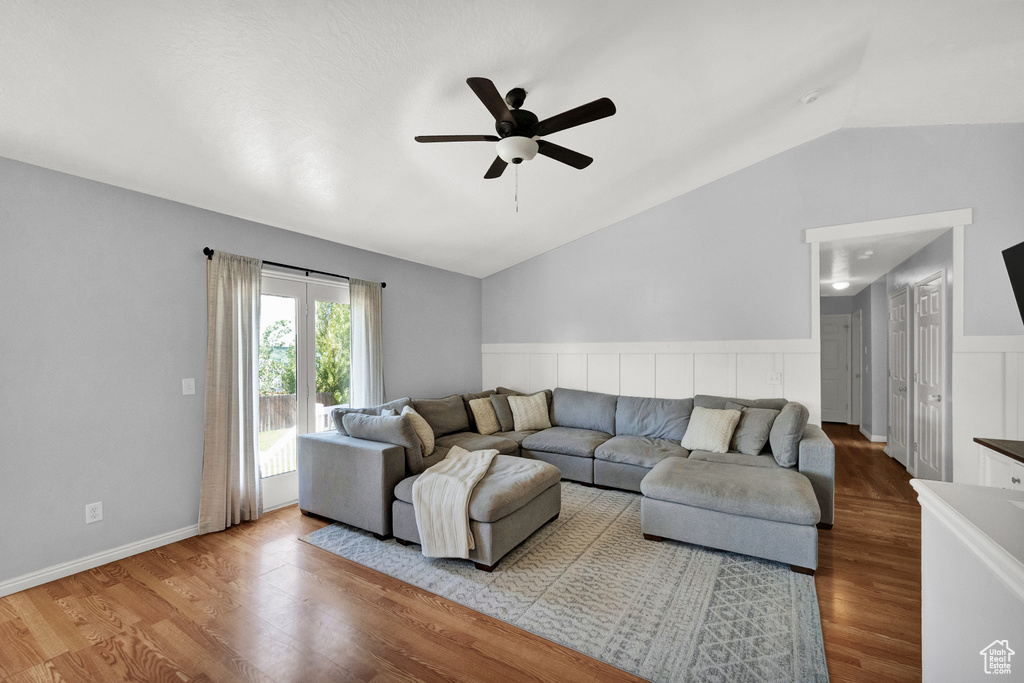 Living room featuring lofted ceiling, wood finished floors, a ceiling fan, and a wainscoted wall